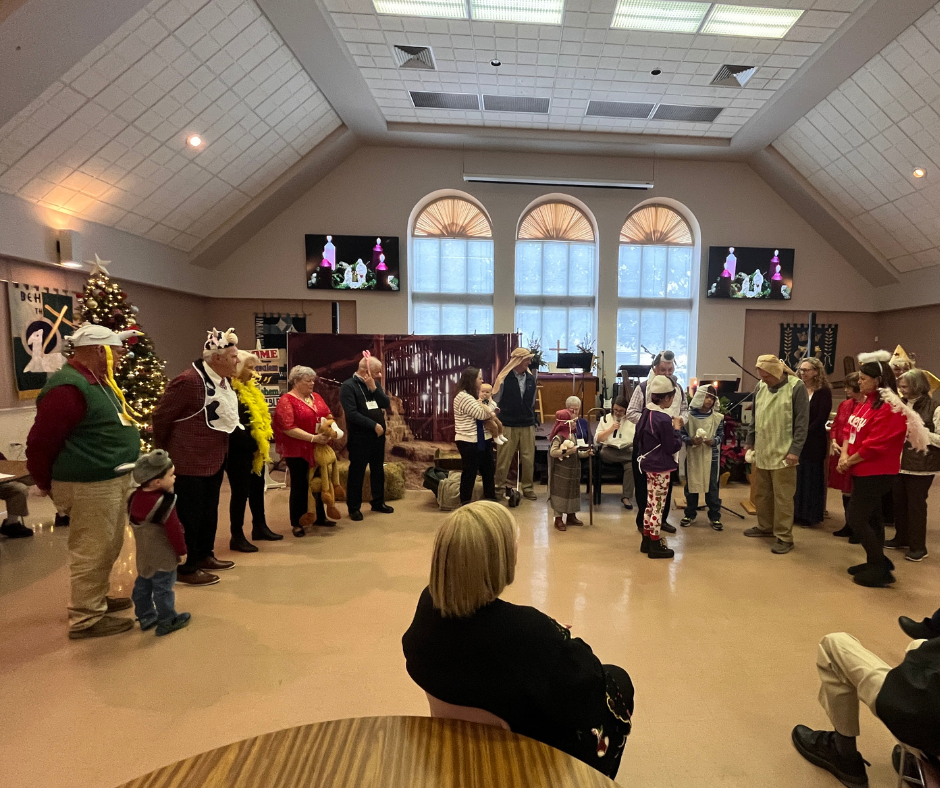 Congregation members in simple costumes gathered in the Fellowship Hall for the paper bag Christmas pageant while others watch from tables