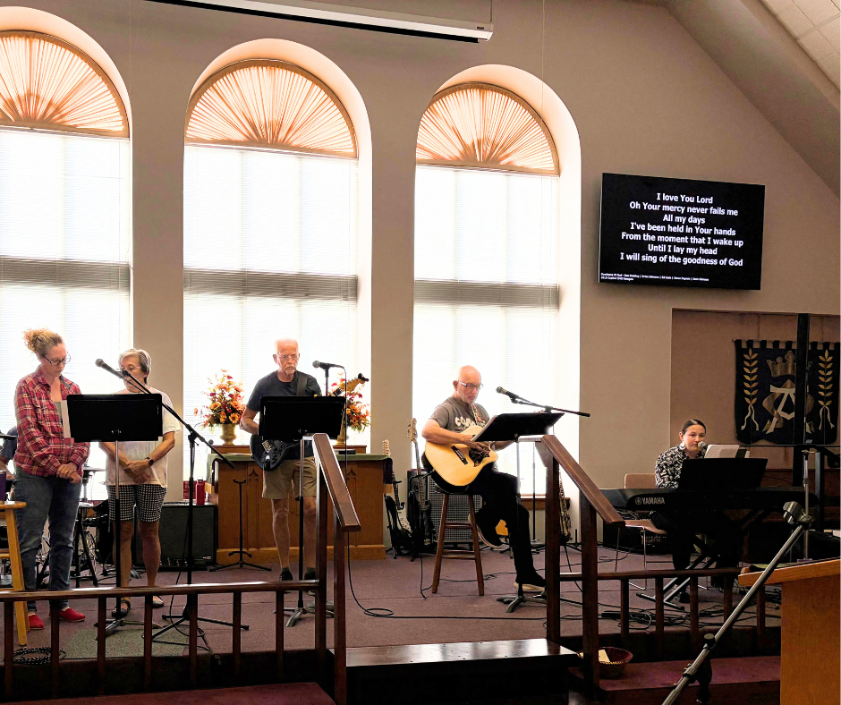 Praise Band members singing and playing guitar, bass and keyboard on the sanctuary stage with lyrics projected overhead