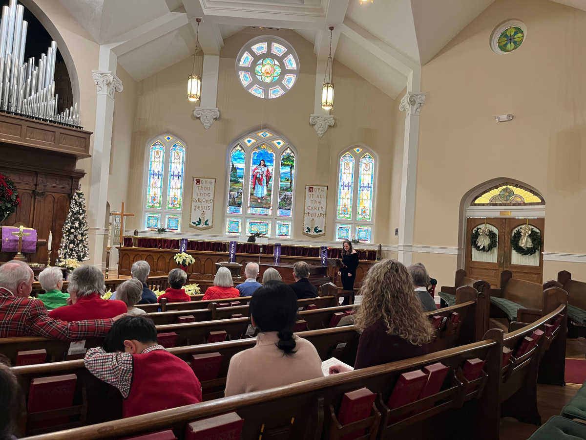 Traditional worship service in historic sanctuary featuring dark wood pews, ornate pipe organ, and stained glass windows